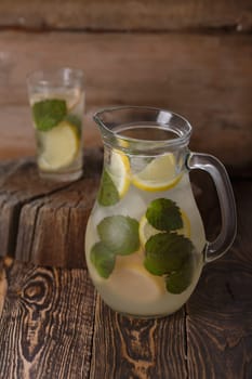 Pitcher of mint lemonade on a wooden table near yellow wild flowers