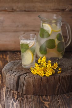 Pitcher of mint lemonade on a wooden table near yellow wild flowers
