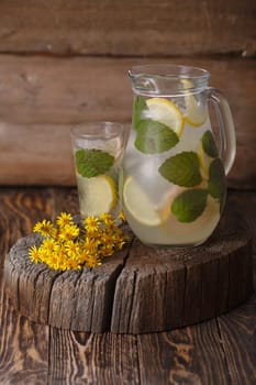 Pitcher of mint lemonade on a wooden table near yellow wild flowers