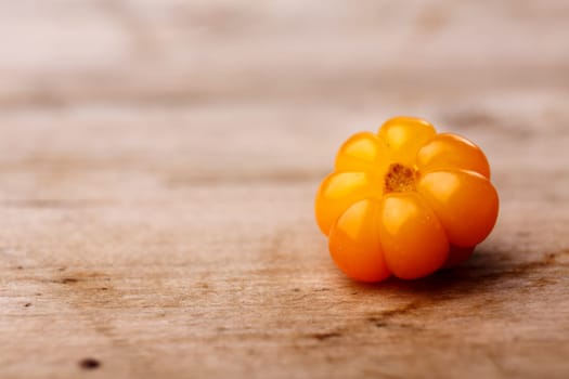 Single cloudberry (moroshka) on a wooden table. Wild northern berry. Shallow depth of field