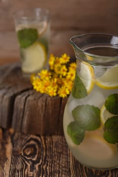 Pitcher of mint lemonade on a wooden table near yellow wild flowers