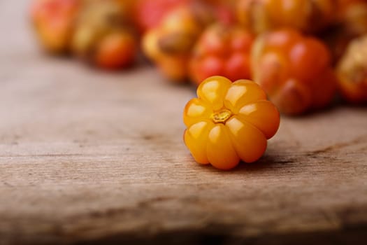 Single cloudberry (moroshka) on a wooden table. Wild northern berry. Shallow depth of field