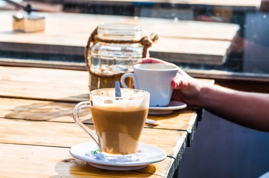 A cup of milk coffee on the table of a beach bar. Background slightly blurred.