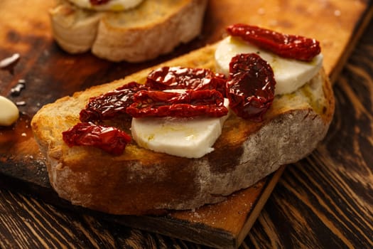 Bruschetta with dried tomatoes, mozzarella, garlic and olive oil. Traditional Italian cuisine sandwich made of grilled ciabatta. Antipasti