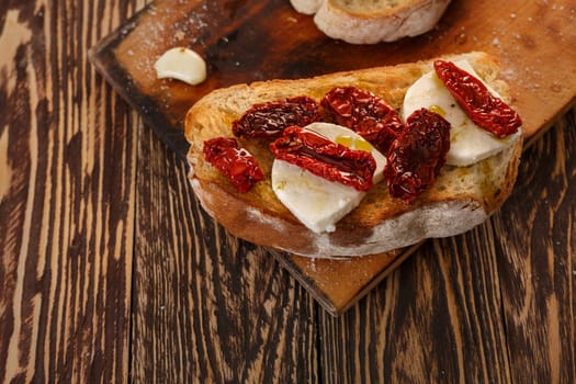 Bruschetta with dried tomatoes, mozzarella, garlic and olive oil. Traditional Italian cuisine sandwich made of grilled ciabatta. Antipasti