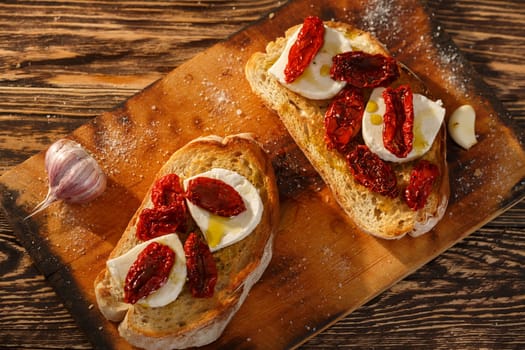 Bruschetta with dried tomatoes, mozzarella, garlic and olive oil. Traditional Italian cuisine sandwich made of grilled ciabatta. Antipasti
