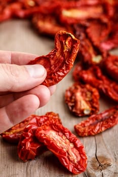 Male hand holding sun dried tomato against  dried tomatoes on wooden table . Selective focus