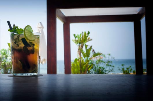 Mojito drink on wood bar with lounger bed and blur beach background