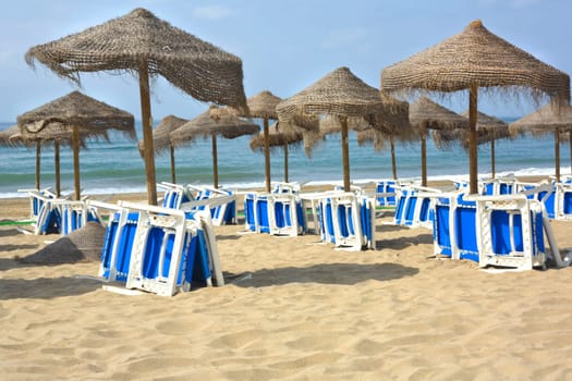 Rustic umbrellas made of natural fibers and sunbeds at Costa del Sol, Spain