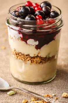 Parfait-style healthy layered breakfast with yogurt,bilberry jam,fresh currant berries,muesli or granola in clear glass on linen clothed table.