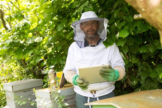 View of a Beekeeper handling a tablet in front of beehives