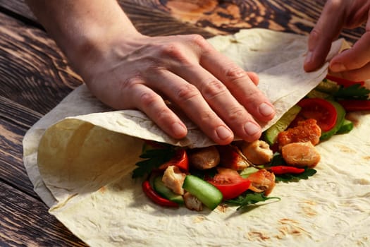 Men's hands wrapping traditional shawarma wrap with chicken and vegetables
