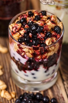 Parfait-style healthy layered snack or dessert with yogurt,bilberry jam,fresh bilberries,puffed honey wheat in  glass on wooden table.