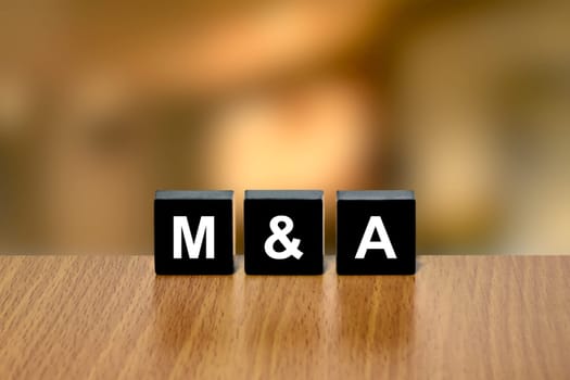 M&A or merger and acquisition on black block with blurred background