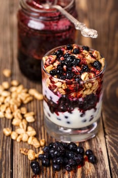 Parfait-style healthy layered snack or dessert with yogurt,bilberry jam,fresh bilberries,puffed honey wheat in  glass on wooden table.