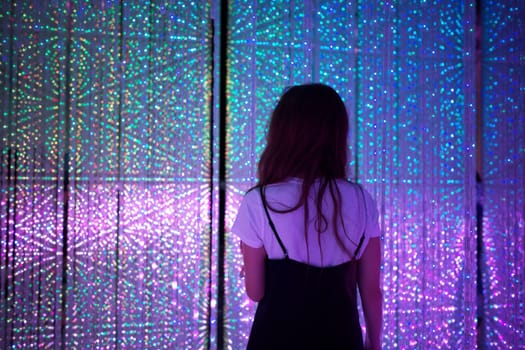 A woman standing amidst a dazzling light exhibit at TeamLab Tokyo, surrounded by vibrant colors and immersive digital art.