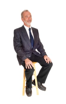 A happy middle age mal in a dress pants, tie and jacket sitting on a chair.with a beard, isolated for white background..