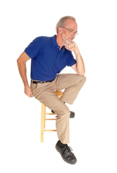 A mal in his fifties' sitting in beige pants and a blue t-shirt on an chair.with his hand on his chin, isolated for white background..