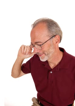 A man in his later years sitting and holding his glasses, in a burgundy.t-shirt, isolated for white background..