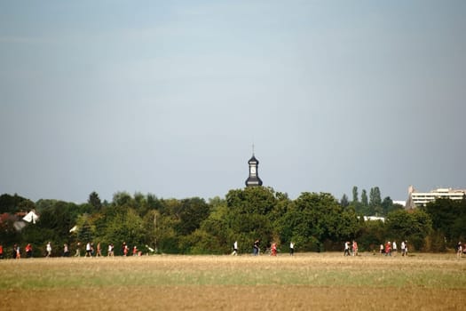 Mainz,Germany - August 28,2015: Fans of the Bundesliga 1. FSV Mainz 05 come from a football match and walk past a church tower on a dirt road on August 28,2015 in Mainz.