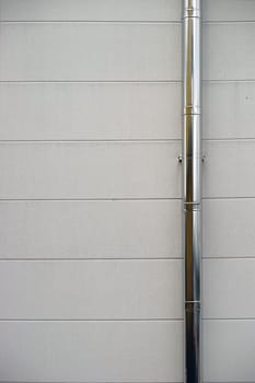 A shiny stainless steel rain gutter on the wall of a building.