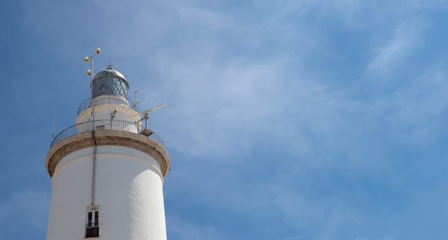 A white whitewashed lighthouse isolated over blue sky with clouds