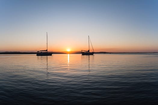 Sunset days end over lagoon landscape with yachts slihoutted on river waters.