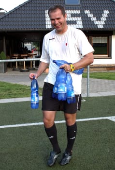 In sports you have to drink a lot and this before the thirst sets in. A coach carries bottles of mineral water onto the football field