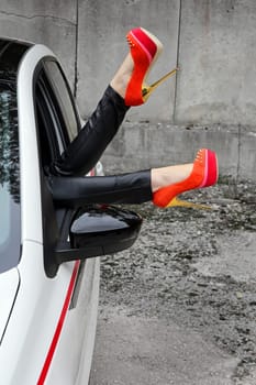A woman stretches her legs out of the window of a car with stick shoes