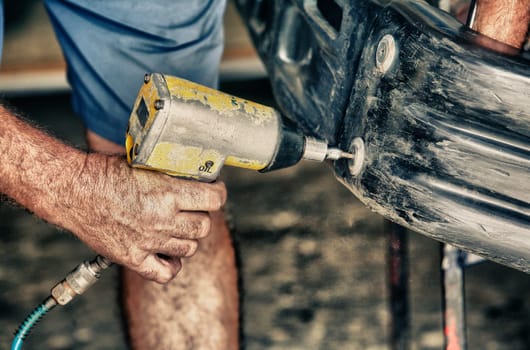 Car mechanic screwing or unscrewing car bumper with oil pressure gun