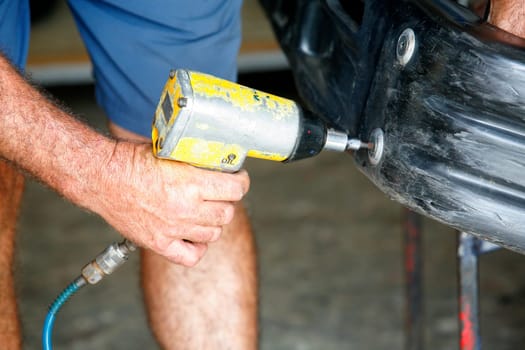Car mechanic screwing or unscrewing car bumper with oil pressure gun