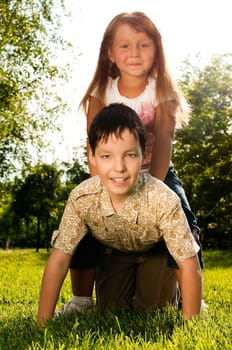 cute little girl sitting on back of her brother, both happy and smiling and looking in camera