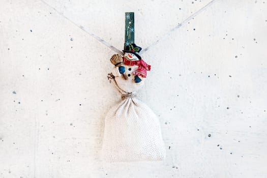 Christmas snowman clothespin hanging at center on clothesline or rope and holding sack on white plaster background