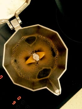 A metal coffeepot brewing Italian espresso coffee over glass-ceramic hob. High view