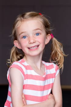 Portrait of a young girl with a grey background. She is smiling and looking at the camera.