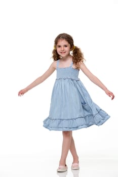 Portrait of a little girl in a summer dress with a white background. She is looking at the camera and smilling.
