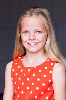 Portrait of a young girl with a grey background. She is looking at the camera and smiling.