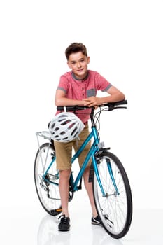 Young boy on a bike on a white background. He is wearing casual clothing and smiling at the camera.