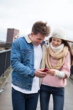 Young couple walking together in the cold weather, looking at a smartphone together.