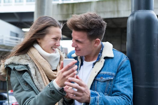 Young couple standing together in the cold weather, looking at a smartphone together