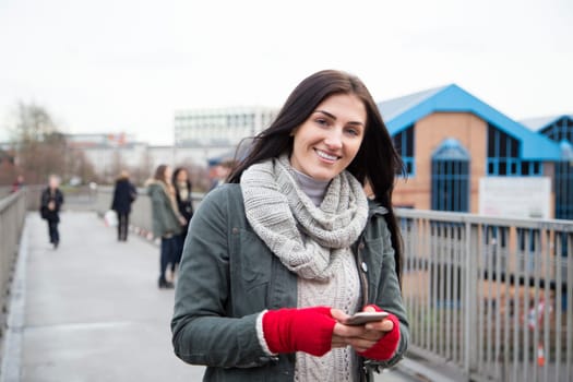 Attractive young woman smiling for the camera with a smartphone in her hands.