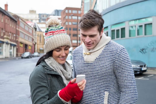 Young couple standing together in the cold weather, looking at a smartphone