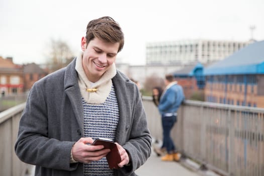 Young adult using a smartphone in the city. A group of people can be seen talking in the background.