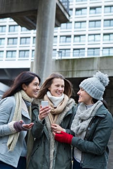 Three young women in the city, looking at something on a smartphone.