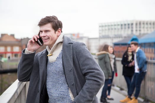Young adult using a smartphone in the city. A group of people can be seen talking in the background.