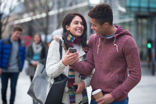 Young couple standing together in the city, looking at a smart phone