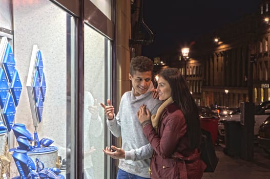 Young couple looking at jewellery through a shop window in the city at evening.