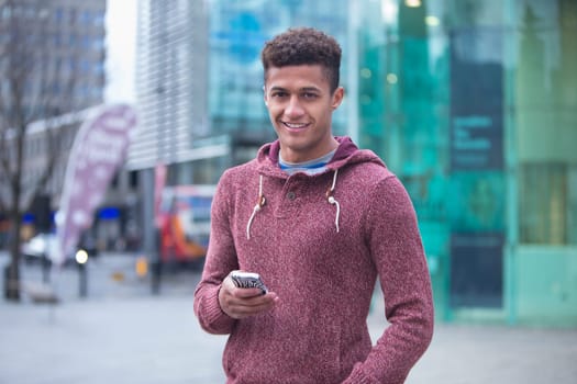 Young, mixed-race man in the city with a smart phone. He is smiling at the camera.