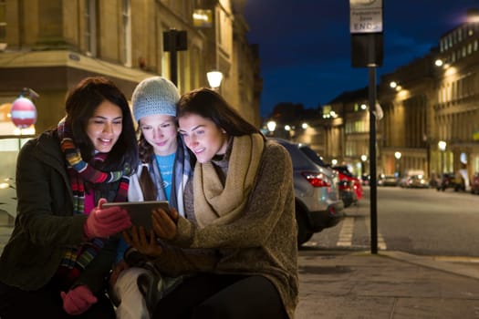 Three friends sitting in the city looking at a digital tablet at evening.
