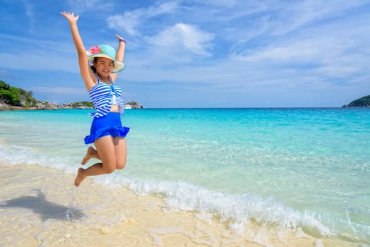 Tourist girl in a blue white striped swimsuit jumping with happy on the beautiful beach and sea during summer at Koh Miang Island, Mu Ko Similan National Park, Phang Nga province, Thailand